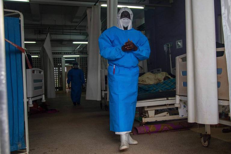 Agente de saúde protegido contra ebola, usa traje azul da cabeça aos pés, com peças brancas para cobrir a cabeça e rosto e botas brancas.