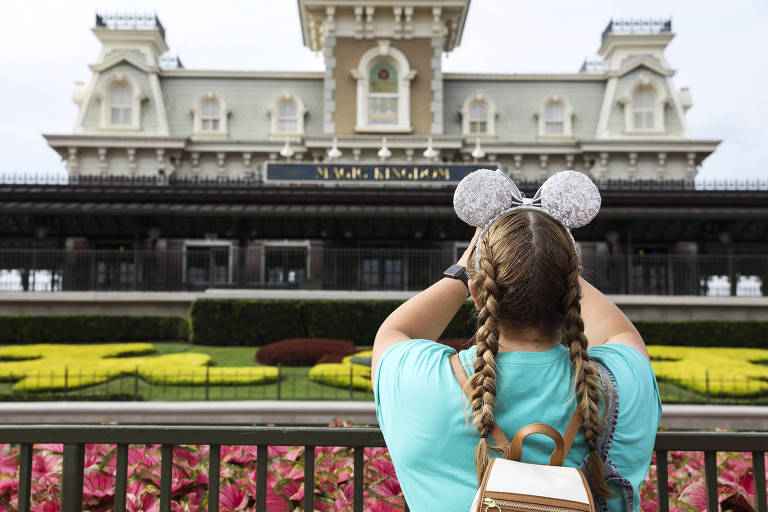 Menina vestida de azul e orelhas de Mickey é vista tirando foto no Magic Kingdom, no Walt Disney World 