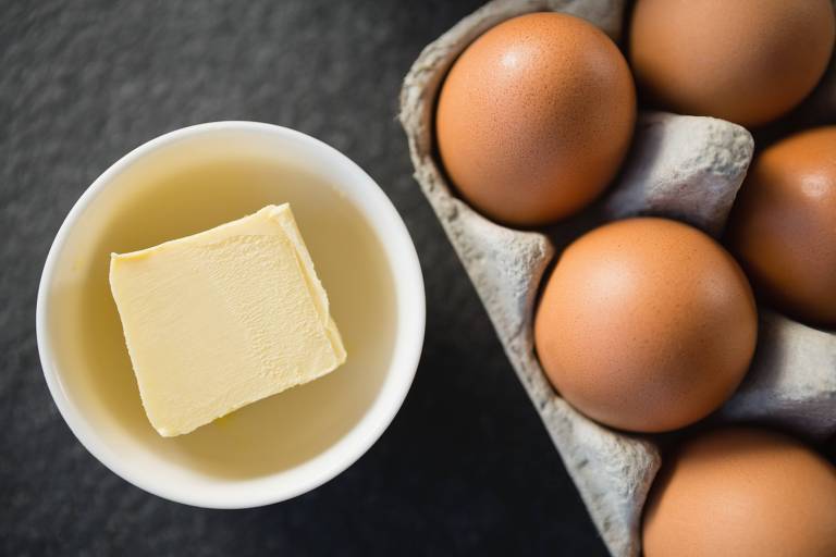 Foto vista do alto de um pote com manteiga e uma caixa de ovos em uma mesa
