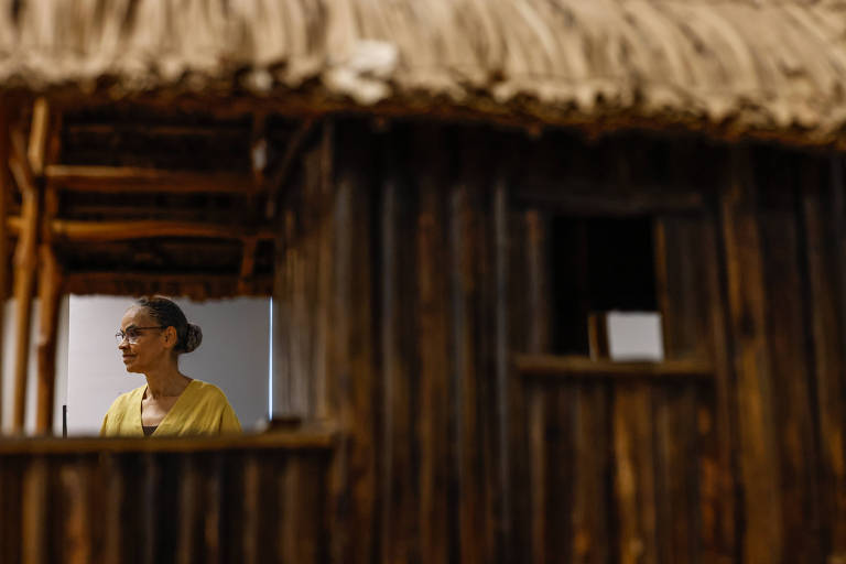 Marina é vista por meio de uma janela da casa de madeira da maquete