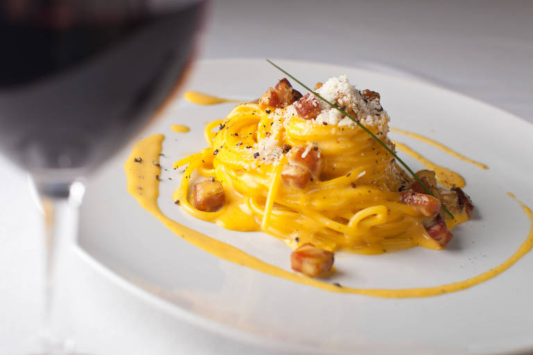 Espaguete à carbonara, feito com ovos, porco e queijo; em primeiro plano, uma taça de vinho tinto