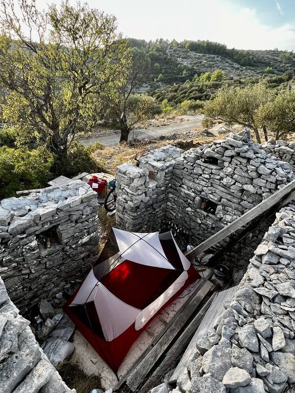 Barraca montada dentro de ruína de pedras em meio a cenário campestre