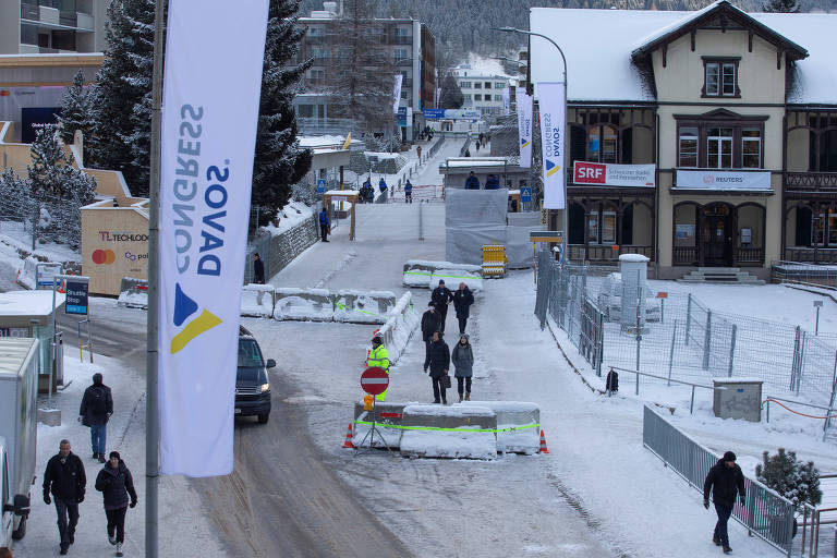 Barreiras de concreto em rua onde pessoas caminham em meio a pouca neve. Há uma placa onde se lê "Davos"