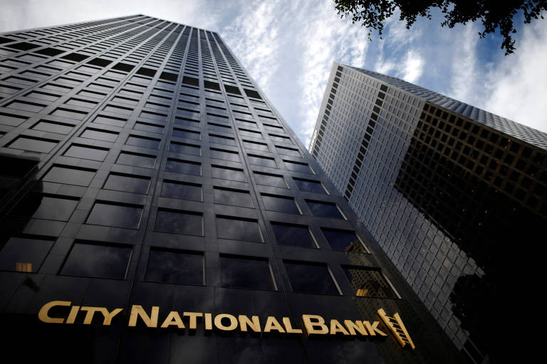 Imagem mostra dois prédios espelhados. Um dele, à esquerda, possui um letreiro com o nome do City National Bank.