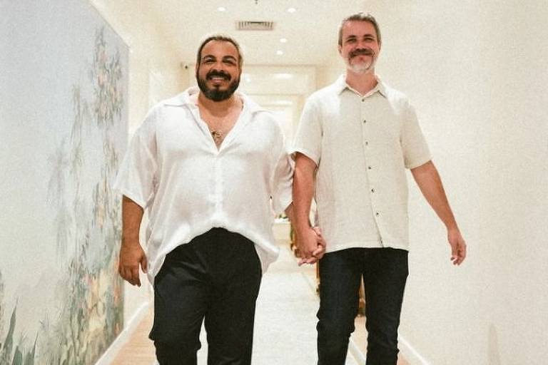 Em foto colorida, dois homens aparecem de mãos dadas em um corredor do hotel Copacabana Palace