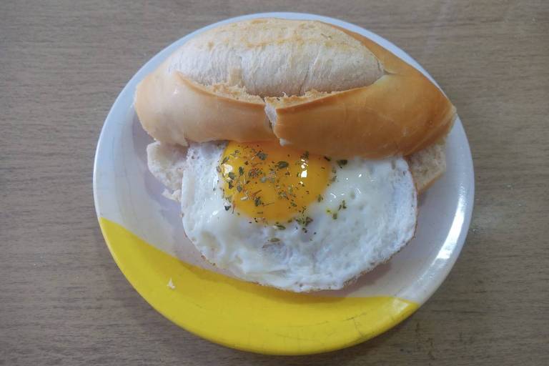 Prato branco e amarelo com um pão com ovo.