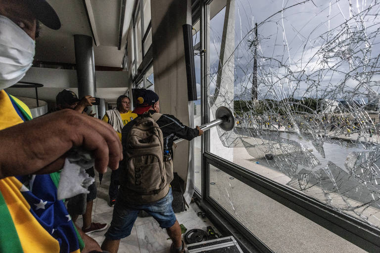 Vândalos golpistas invadem a praça dos Três Poderes e depredam os prédios. Na imagem, homem quebra janela do Palácio do Planalto