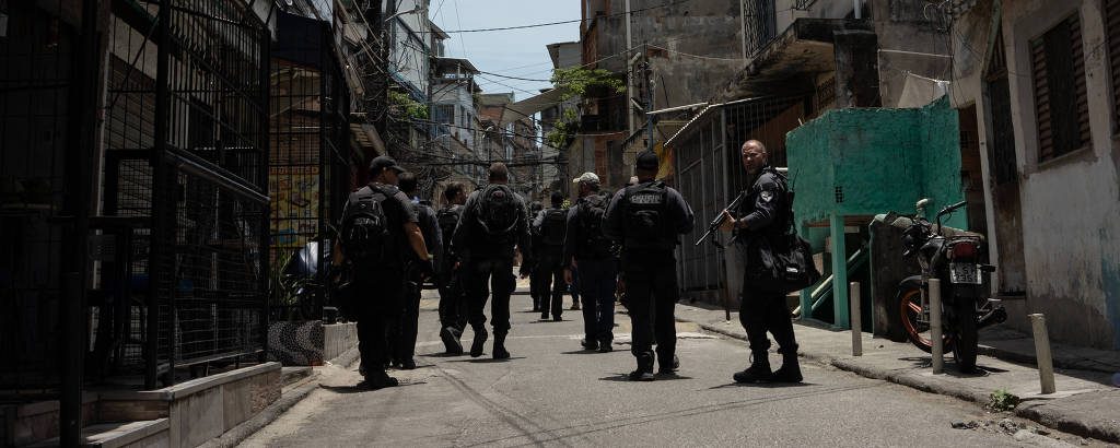 Grupo de policiais caminham de costas por rua da favela