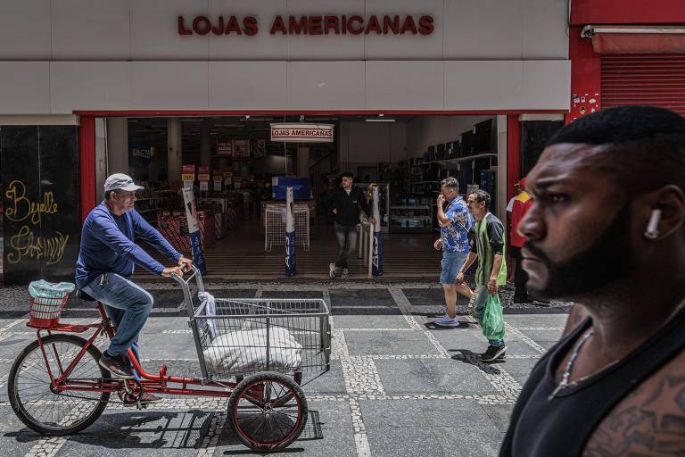 Homem passa de triciclo em calçadão, em frente a loja da Americanas