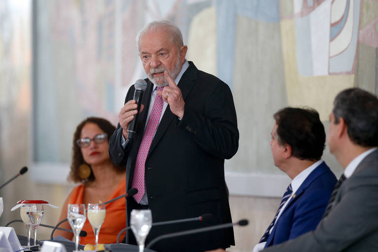 Lula fala de pé, gesticula ao lado de três ministros sentados.