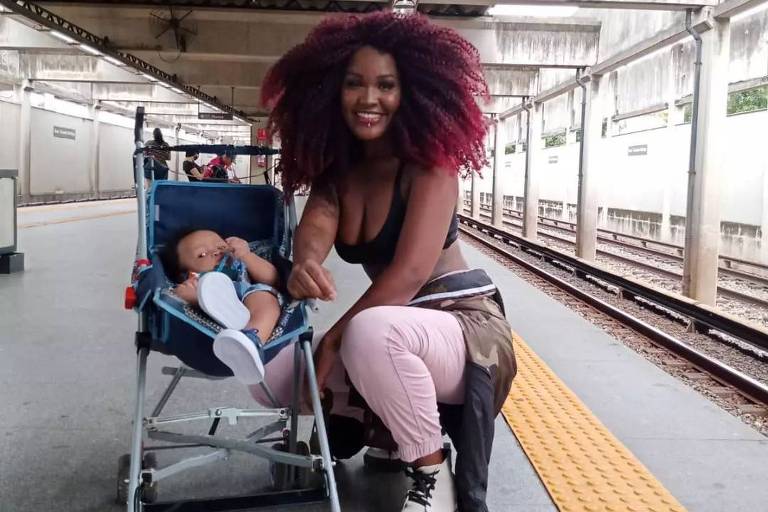 Mulher negra ajoelhada ao lado de carrinho de bebê em estação de metrô
