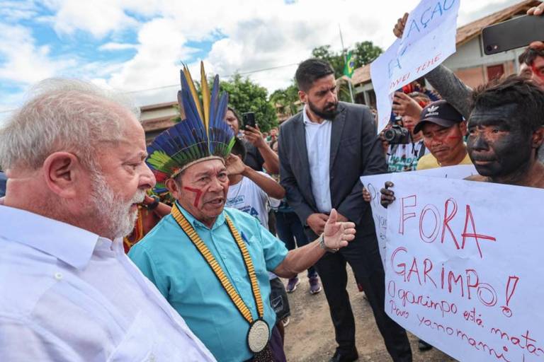 O presidente luiz inácio lula da silva olha para cartaz que diz "fora garimpo"  exibido por indígena à sua frente 