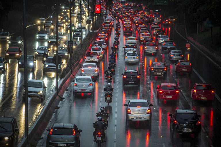 Filas de carros e motos com faróis acesos no início da noite em avenida