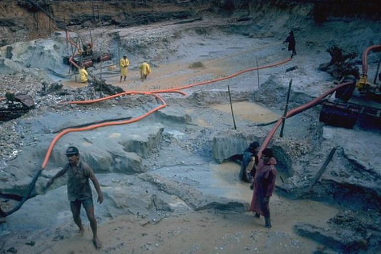 foto mostra operação de garimpo com lama, terra cinza, mangueiras de água e trabalhadores