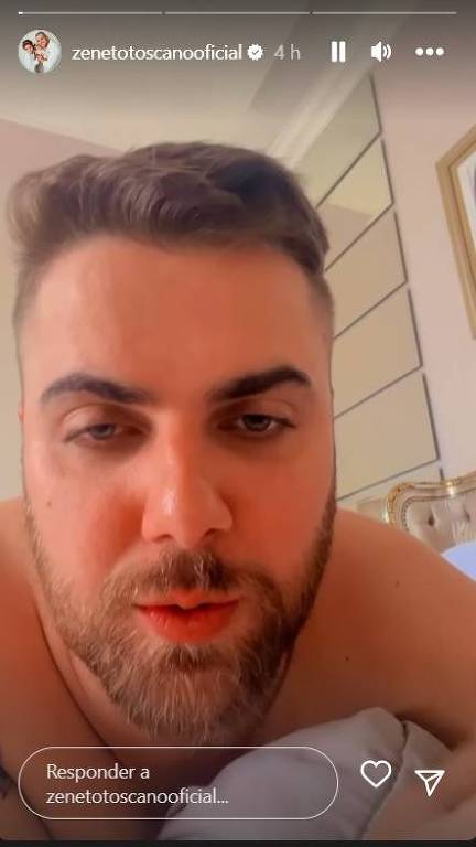 Em foto colorida, homem aparece deitado em uma cama e faz um vídeo explicando sobre o cancelamento de um show