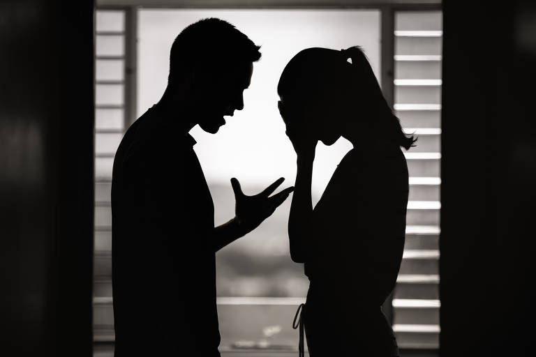 Homem gesticula agressivamente diante de mulher, que coloca a mão no rosto. Eles estão contra a luz e apenas seus vultos podem ser vistos