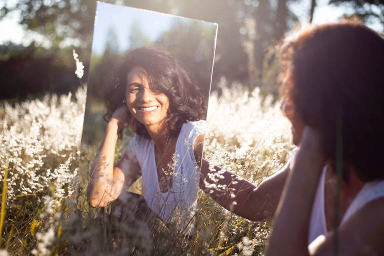 Uma pessoa sentado num campo se vê no espelho e sorri
