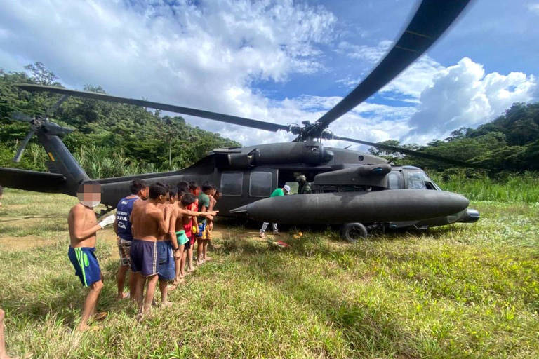 Pessoas fazem fila para receber comida que está sendo distribuída em um helicóptero pousado na grama