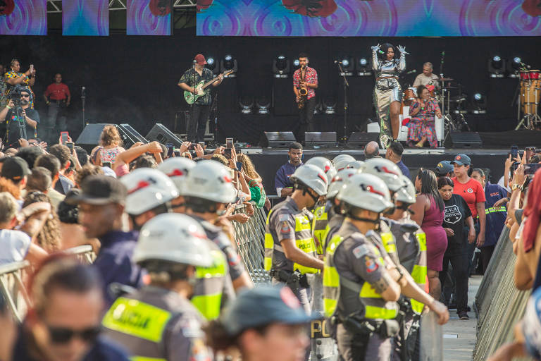 foto mostra policiais em meio a plateia, eles formam um  linha que vai até o fundo da foto. em segundo plano está o palco com os artistas