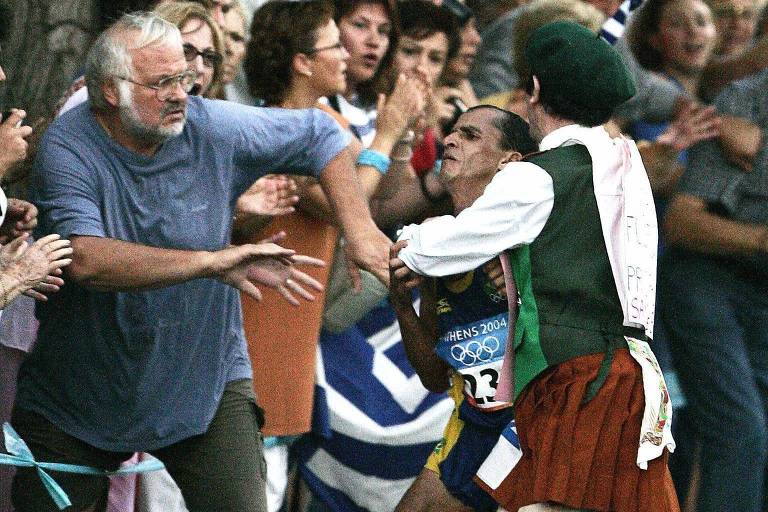 Polyvios Kossivas (à esq) ajuda o brasileiro Vanderlei Cordeiro de Lima a se livrar do irlandês Cornelius Horan durante a maratona das Olimpíadas de Atenas, em 2004