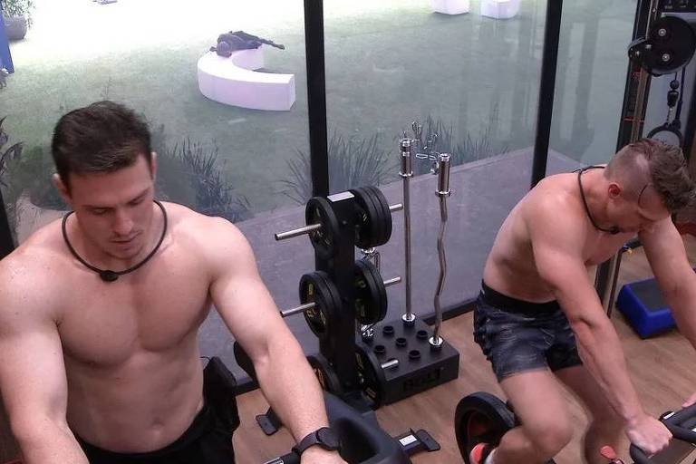 Em foto colorida, dois homens malham em uma academia