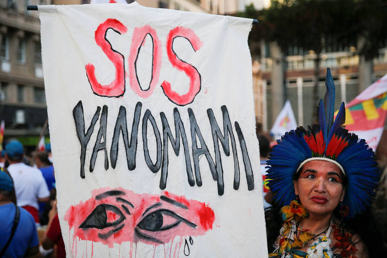 Mulher segura faixa branca que diz: "SOS Yanomani"