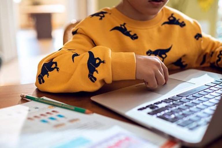 Criança com blusa amarela com desenhos pretos, usando um computador sozinha