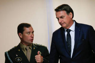 Brazil's President Jair Bolsonaro talks with army major, Mauro Cid after a meeting at the Planalto Palace in Brasilia