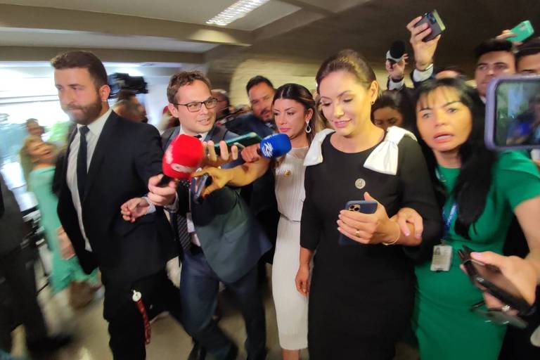 Michelle Bolsonaro caminha por um corredor do Senado, acompanhada por assessores e jornalistas. 