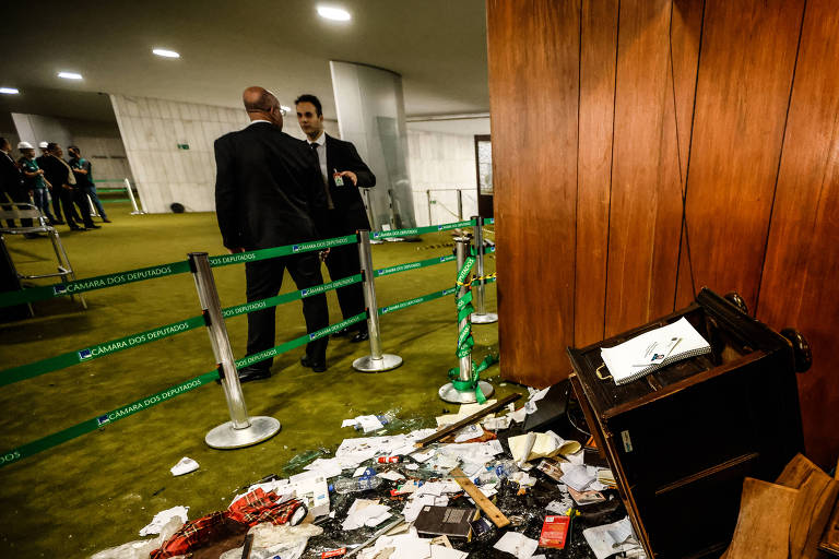 Imagem mostra parte do salão verde, há dois seguranças ao fundo e, no primeiro plano, um amontoado de papeis e documentos no chão