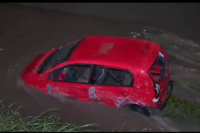 A imagem mostra um carro vermelho dentro de um rio