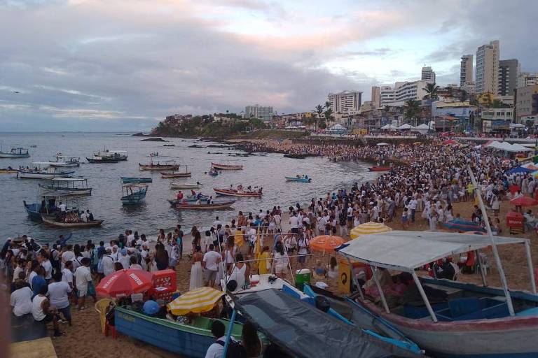 Praia de Santana tomada por pessoas vestidas de branco e barcos no mar