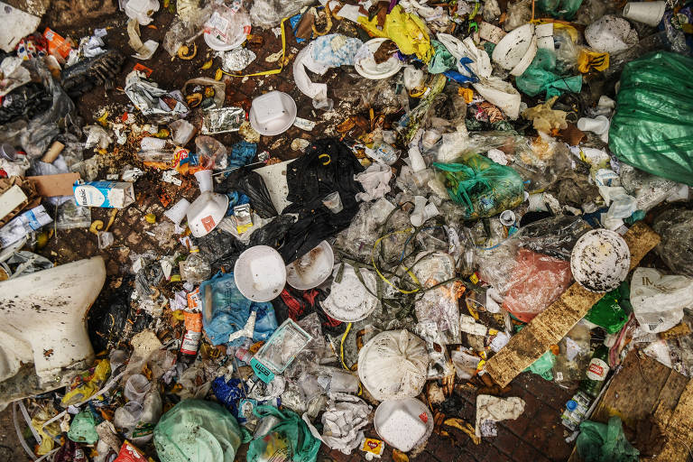 Amontoado de lixo visto de cima, com marmitas e tampas de isopor, sacos plásticos, sujeira e vaso sanitário