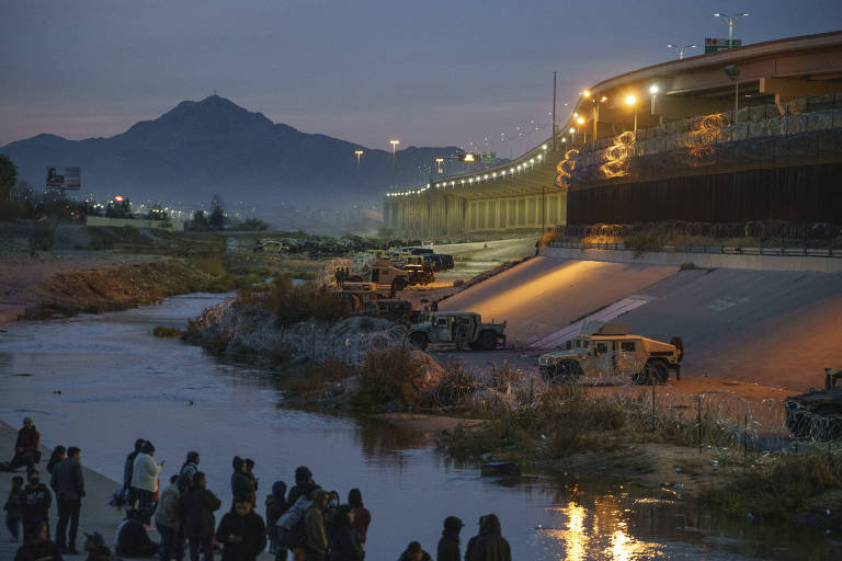 Migrants in Juarez, Mexico, at left, gather across the Rio Grande from a blockade created to halt further border crossings by Texas National Guard soldiers, part of a ?contingency border force,? on Tuesday, Dec. 20, 2022. One of the most expansive immigration restrictions along the U.S.-Mexico border, known as Title 42, remained in force on Tuesday evening as lawyers for the Biden administration, migrant rights activists and Republican governors debated its continued use in written briefs submitted to the Supreme Court. (Paul Ratje/The New York Times)