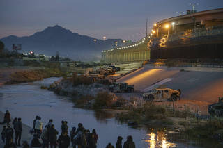 Migrants in Juarez, Mexico, at left, gather across the Rio Grande from a blockade created to halt further border crossings by Texas National Guard soldiers, part of a ?contingency border force,? on Tuesday, Dec. 20, 2022. (Paul Ratje/The New York Times)