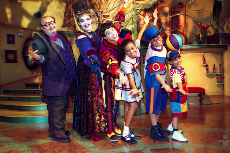 três atores adultos e três crianças posam para foto caracterizados como os personagens da serie infantil dentro do estudio