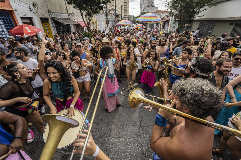 foto mostra cortejo de carnaval, com pessoas tocando instrumentos e multidão acompanhando 