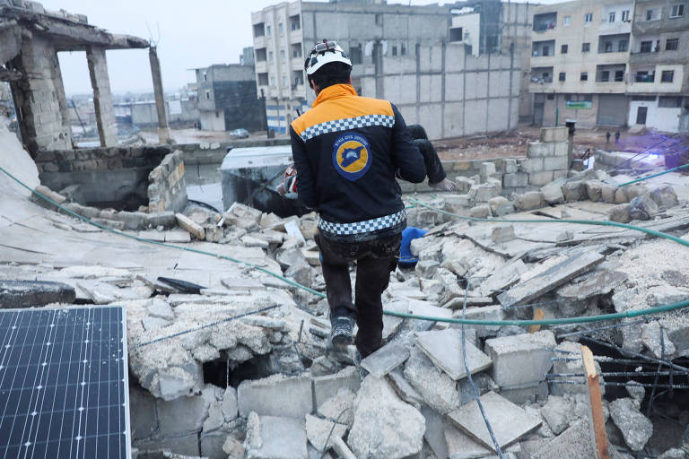 Bombeiro carrega criança em meio a escombros de prédio desabado após terremoto, em Azaz, na Síria