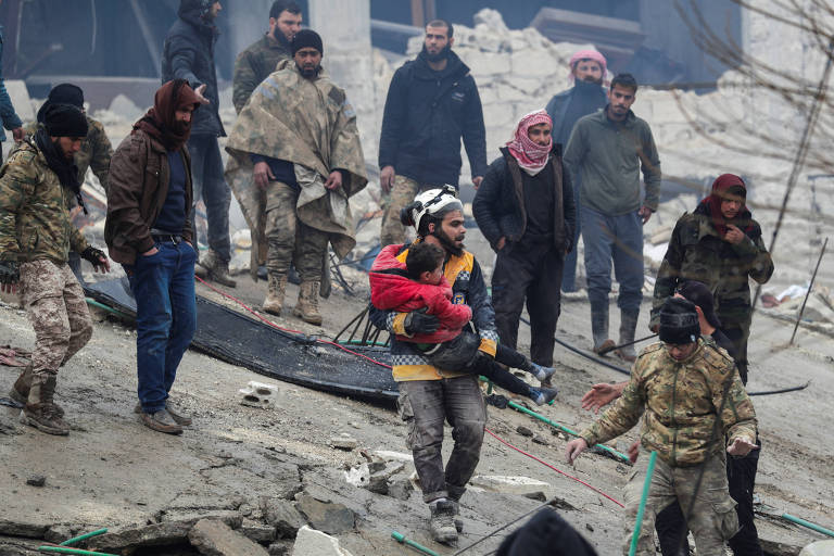 Socorrista carrega criança encontrada em escombro após terremoto na cidade síria de Jandaris, controlada por rebeldes