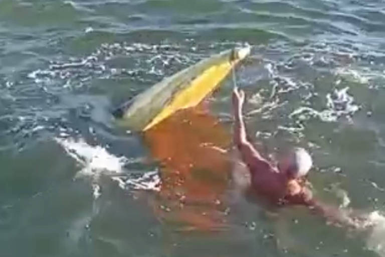 foto mostra homem no mar segurando cabo preso à canoa