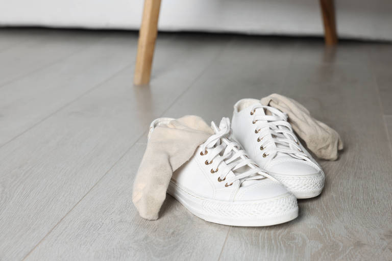 Um par de tenis branco no chão, sob meias usadas