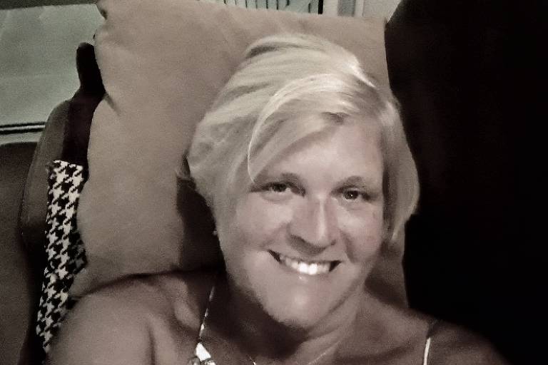 Mulher loira sentada em sofá e sorri para câmera