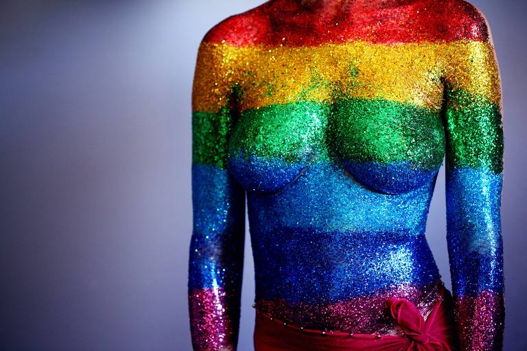 An 18 year old person covered in rainbow body glitter in support of the LGBTQ community and to celebrate gay pride 2018. We used a synthetic cosmetics brush to paint clear hair gel on their torso and then they laid down and I sprinkled the glitter on their body, one stripe at a time. We were able to touch up by dabbing more glitter on after they stood up. We used water-proof adhesive bandages to cover the sensitive areas on the chest and the belly-button.