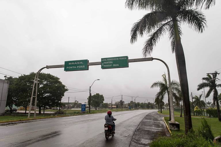 Imagem colorida mostra estrada com duas placas verdes, uma está escrito Pedro Juan Caballero e na outra a Ponta Porã
