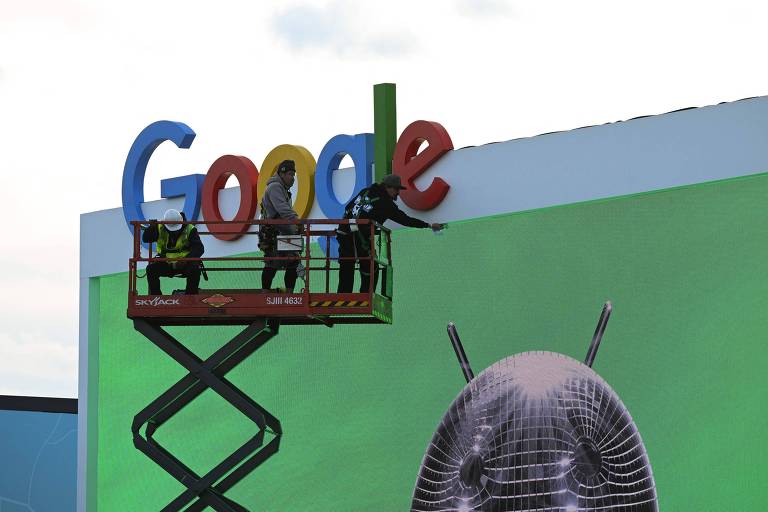 Pessoas em cima de um andaime são vistas retocando um outdoor dp Google com uma parede verde 