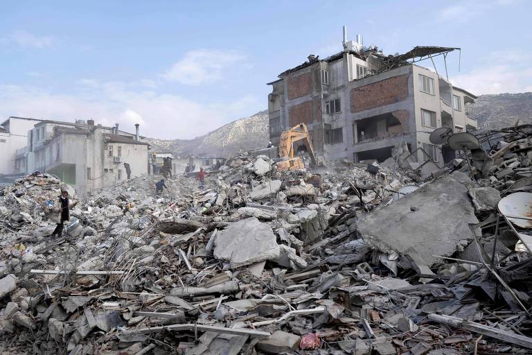 Pessoas caminham sobre os destroços de edifícios colapsados em Hatay, na Turquia