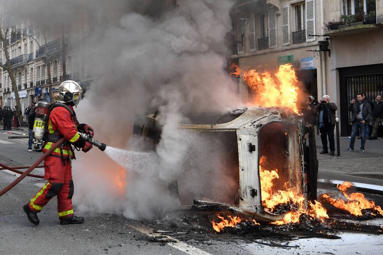 Bombeiro tenta apagar fogo de carro incendiado em Paris durante os protestos
