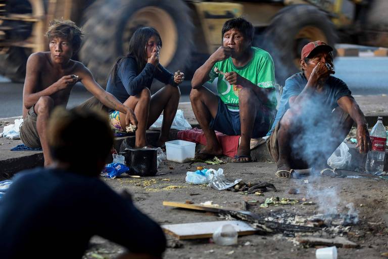 À beira da calçada, em Boa Vista, capital de Roraima, cinco indígenas da etnia Yanomami se alimentam.