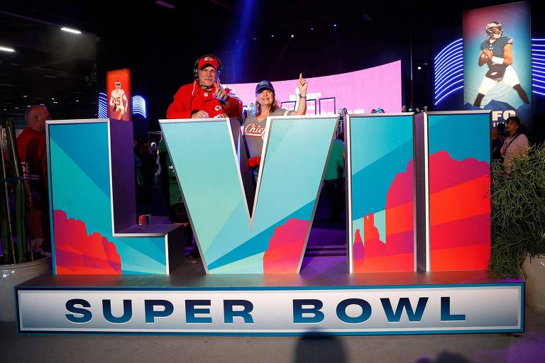 Um torcedor vestido como o técnico do Kansas City Chiefs, Andy Reid, posando ao lado de um totem do Super Bowl LVII e da esposa