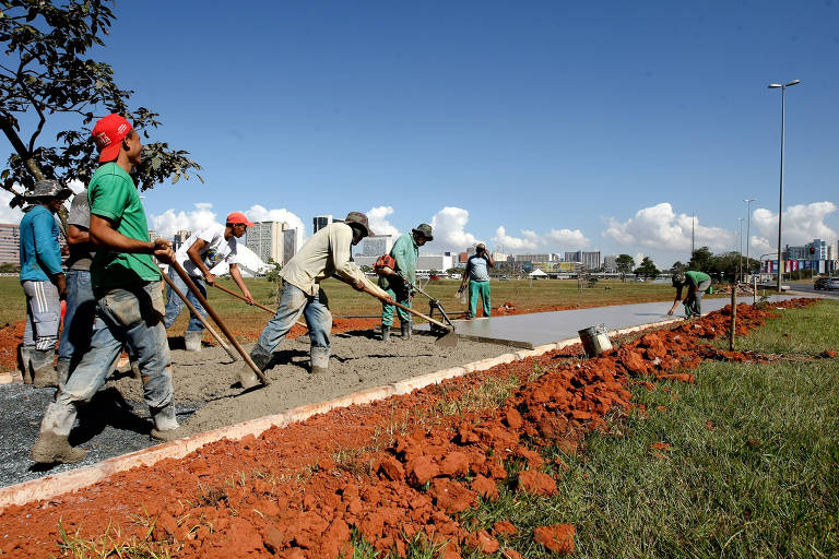 Homens usam pás para espalhar concreto num canteiro de obras a céu aberto